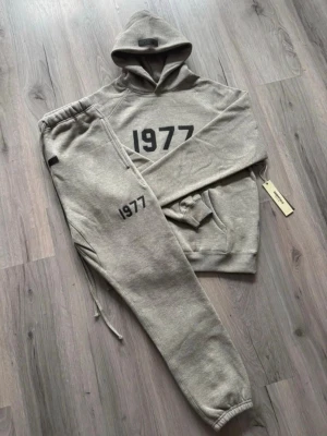 🩶1977 tracksuit grå färg🩶 - Säljer ett set med grå hoodie och matchande mjukisbyxor med trycket '1977' på både tröjan och byxan. Setet har en avslappnad passform, huva och resår i midja och benslut. Perfekt för chill dagar hemma eller när du vill vara bekväm.  Tar emot rimliga bud. För mer info kom privat.