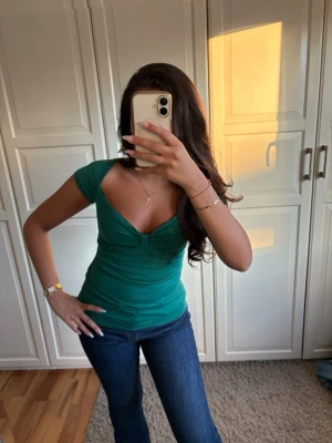 Grön v-ringad topp med kort ärm - Snygg grön topp med djup v-ringning och korta ärmar. Figurnära passform som framhäver midjan. Perfekt till jeans eller kjol för en trendig look.