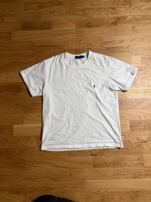  Polo Ralph Lauren vit tröja - Klassisk vit t-shirt från polo Ralph Lauren i bomull med korta ärmar och rund hals. På bröstet finns en liten broderad logga i mörkblått som ger en stilren touch. Perfekt basplagg för alla tillfällen och enkel att matcha med andra plagg.