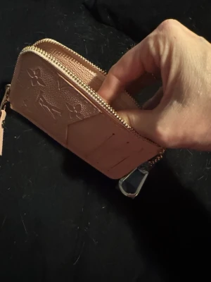 Rosa plånbok med dragkedja - Snygg rosa plånbok i läderimitation och dragkedja. Plånboken har ett fack på utsidan och en metallhake för att fästa i nyckelknippa eller väska. Perfekt storlek för kort och mynt.