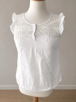 MassimoDutti blus - (Designer) Söt vit blus med spets upptill och volangärmar. Blusen har rund halsringning, knappar framtill och är ärmlös med fina spetsmönster både fram och bak. Perfekt för en fräsch och somrig look. Ej stretchigt material! (Bomull)