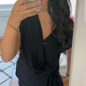 Svart blus med knyt - Snygg svart blus med knyt i midjan och v-ringad hals. Blusen har korta ärmar och en stilren, enkel design som passar perfekt när du vill känna dig både bekväm och chic. Säljer då den inte kommer till användning. Är i storlek xs men skulle säga att den passar xs/s.