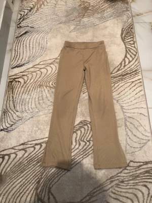 Beige ribbade leggings med utsvängda ben för barn - Säljer ett par beige leggings från 157.NEW med ribbad struktur och utsvängda ben. De har bred resår i midjan och är tillverkade i ett mjukt, stretchigt material som sitter skönt. Perfekta för en avslappnad och trendig look.