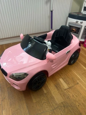 Rosa elbil för barn - Säljer en snygg rosa elbil för barn med svarta detaljer och sportig design. Bilen har svarta säten, ratt och vindruta samt stora svarta hjul. Perfekt för inomhuslek eller ute på gården. Laddas enkelt och har plats för ett barn.
