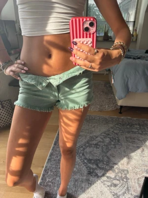 Mintgröna fransiga shorts - Snygga mintgröna shorts med fransig kant och låg midja. Perfekta för varma dagar och ger en avslappnad vibe. Gjorda i bomull för en skön känsla. Lätta att matcha med crop tops eller linnen.