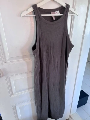 Grå/brun ribbad långklänning H&M - Säljer en enkel och snygg grå/brun långklänning från H&M. Klänningen är ribbad, ärmlös och har en rund halsringning. Perfekt för sommardagar eller att styla med en jacka. Materialet är mjukt och stretchigt, vilket gör den bekväm att bära.