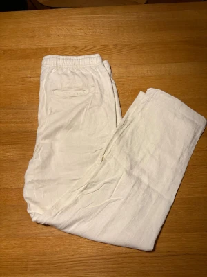 Linnebyxor  - Säljer ett par vita linnebyxor med avslappnad passform och resår i midjan. Byxorna har en bakficka och är tillverkade i ett lätt och luftigt linnetyg, perfekta för en chill och stilren look.