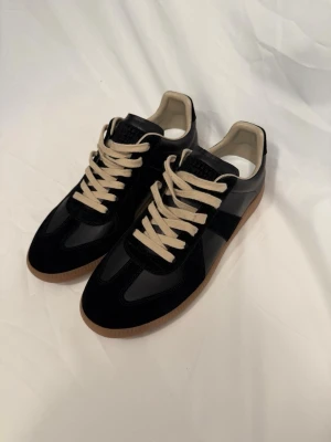 Maison marigela - Maison Margiela sneakers i svart skinn och mocka med beige detaljer och snörning. Klassisk rund tå och platt gummisula i brunt. Är du intresserad av fler bilder eller vill veta mer, är det bara att höra av dig!
