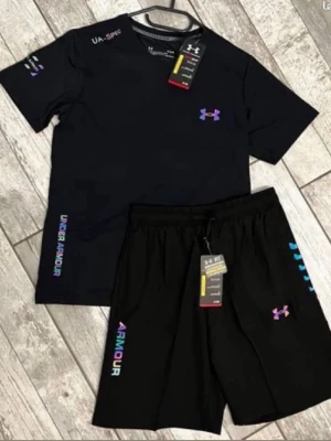 Svart träningsset från Under Armour - Snyggt svart träningsset från Under Armour med t-shirt och shorts. Båda plaggen har färgglada loggor och textdetaljer i lila, blått och rosa. Perfekt för gymmet eller löprundan. Materialet är lätt och andas, vilket gör det bekvämt under träning.