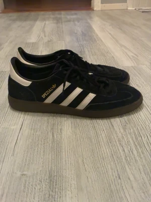 Adidas Spezial svarta sneakers - Svarta Adidas Spezial sneakers storlek 48 2/3 med klassiska vita ränder på sidorna och gummisula. Ovandelen är i mocka och textil, med guldfärgad 'Spezial'-logga på sidan. Knappt använda och nypris över 1000kr.. 