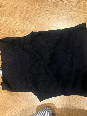 Svart ribbad ärmlös topp Divided - Säljer en svart ribbad topp från Divided H&M. Toppen är ärmlös och har en enkel, tight passform som passar perfekt till alla dina outfits. Materialet är mjukt och stretchigt för extra komfort.