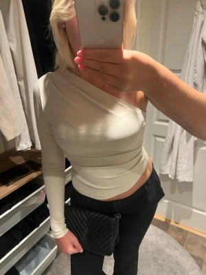 Vit oneshoulder topp med lång ärm - Snygg vit oneshoulder topp med lång ärm och tight passform. Toppen är croppad och har en stilren look som passar perfekt till både jeans och kjol.  