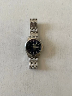 Silverfärgad klocka från Festina - Stilren klocka från Festina med silverfärgad länk i metall och svart urtavla. Klockan har tydliga markeringar, datum- och veckodagsvisning samt klassisk design. Perfekt accessoar för dig som gillar tidlös stil.