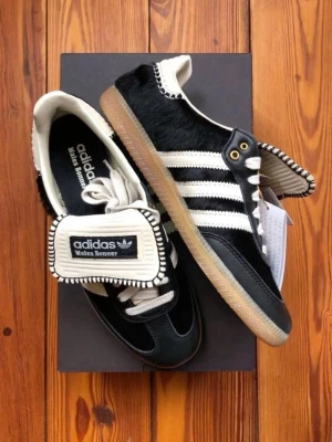 Adidas Wales Bonner svart/vit sneaker - Unika Adidas Wales Bonner sneakers i svart och vitt med klassiska tre ränder på sidan. Skorna har detaljer i mocka och läder, samt en speciell tunga med Wales Bonner-logga och kontrastsömmar. Yttersulan är i gummi och ovandelen har inslag av pälsimitation.