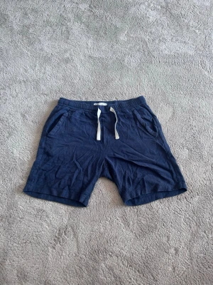 Mörkblå shorts med snörning - Snygga mörkblå shorts med vit snörning i midjan och två sidofickor. Shortsen har en avslappnad passform och är tillverkade i ett mjukt bomullstyg, perfekta för varma dagar.