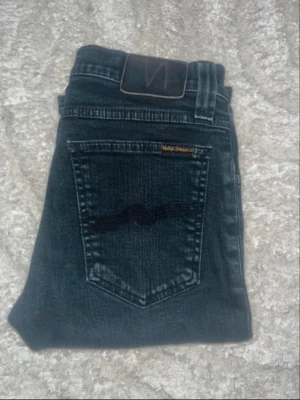 Nudie jeans  - Snygga mörka jeans från Nudie Jeans, modell tight long John. Midja 34cm, längd 101cm. JAG SKICKAR EJ FLER BILDER NÄR JAG BÄR JEANSEN! för bättre inblick i passformen rekommenderar jag att googla på modellnamnet. För storleksguide kolla måtten noggrant då jeansen alltid kan vara uppsydda heller krympta och jag ej tar emot returer :) s6,4
