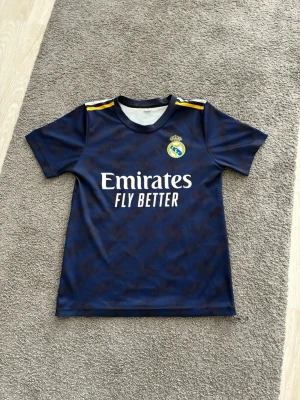 Real Madrid Bellingham matchtröja - Mörkblå Real Madrid matchtröja med namnet Bellingham på baksidan tröjan har en liten orange fläck på märket fly better
