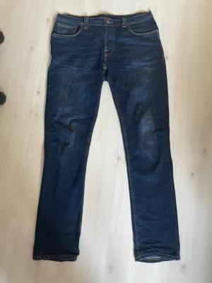 Mörblå slim fit jeans Nudie  - Säljer ett par mörkblå nudie jeans med klassisk femficksdesign. Jeansen har kontrastsömmar och en snygg tvättad look. Perfekta för dig som gillar en enkel och stilren stil. Storlek W 34 L 32 modellen är Grim Tim slim/straight