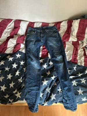 Blå slim fit jeans från Replay - Snygga blå slim fit jeans från Replay med slitna detaljer och klassisk femficksdesign. Jeansen har dragkedjegylf och metallknapp i midjan. Perfekta för en avslappnad och trendig look.