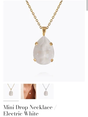Mini Drop halsband i vitt från Caroline Svedbom - Helt nytt, Elegant halsband med droppformad vit kristall och guldfärgad kedja från Caroline Svedbom. Hänget har en elektriskt vit ton och infattning i guldpläterad metall. Perfekt för dig som gillar stilrena och trendiga smycken.