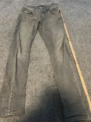 Gråa slim fit jeans från Replay - Snygga gråa slim fit jeans från Replay med klassisk femficksdesign och svarta detaljer vid fickorna. Jeansen har en något tvättad look och raka ben. Perfekta för dig som gillar en stilren och modern vibe.