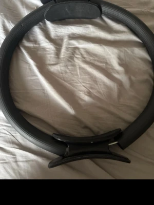 Svart pilatesring med handtag - En svart pilatesring med bekväma handtag på sidorna, perfekt för styrketräning, stretching och pilatesövningar. Ringen är tillverkad i slitstarkt material och har en rund form som ger bra grepp under träningen.