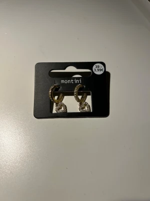 Guldiga örhängen med hjärtan - Snygga guldiga örhängen från Montini med små gnistrande stenar på ringen och en hängande pärldetalj. Perfekta för att ge din look lite extra bling. Klassisk och trendig design som passar till många stilar. Oanvända.