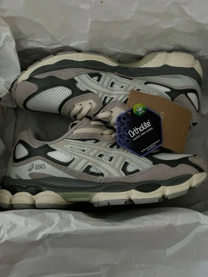 Asics GEL - NYC  - Snygga Asics sneakers i beige, grått och vitt med meshpaneler och detaljer i mocka och syntet.  Skorna är helt nya. Kommer i storlek 42. 