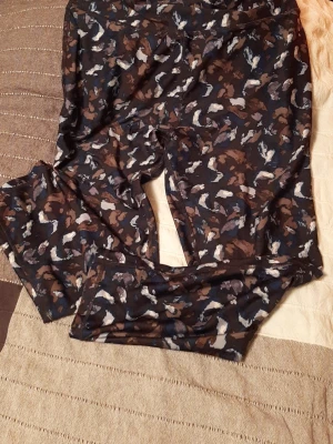 Mönstrade leggings i bruna toner - Säljer ett par leggings med coolt abstrakt mönster i bruna, svarta, vita och blå nyanser. De är stretchiga och har en bekväm passform med elastisk midja. Perfekta för dig som gillar att sticka ut med din stil och vill ha något mjukt och skönt.