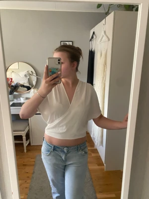 Vit omlott croppad topp - Säljer en vit croppad omlott-topp med korta ärmar. Toppen har en v-ringad design och är tillverkad i mjukt bomullsmaterial. Perfekt för dig som gillar en enkel och stilren look med lite edge.