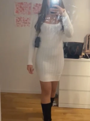 Vit ribbad långärmad klänning - Snygg vit ribbad klänning med lång ärm och fyrkantig urringning. Modellen är kroppsnära och kort, perfekt för dig som gillar en stilren och trendig look. Klänningen är stickad i ett mjukt material som sitter bekvämt och framhäver figuren. Aldrig använt.