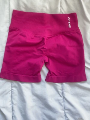 Rosa impact shorts  DFYNE - Snygga rosa seamless shorts från DFYNE med hög midja och ribbad linning. Perfekta för träning eller chill, med stretchigt material som sitter skönt på kroppen. Logga framtill och baktill i vitt.
