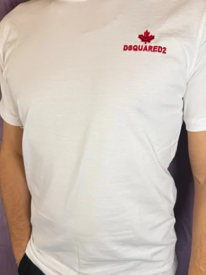 Vit Dsquared2 t-shirt med broderi - Vit t-shirt från Dsquared2 med röd broderad logotyp och lönnlöv på bröstet. Klassisk passform och korta ärmar, tillverkad i mjuk bomull som känns skön mot huden. Perfekt för dig som gillar stilrena och trendiga plagg.