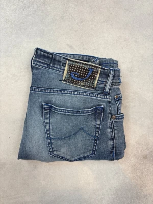 Blå raka jeans från Jacob Cohën - Snygga blå jeans från Jacob Cohën med raka ben och klassisk femficksmodell. Jeansen har en cool patch med ett stort J på bakfickan och är gjorda i mjukt denimtyg. Perfekta för dig som gillar en avslappnad men stilren look.