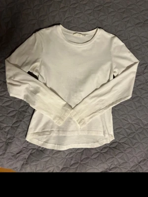 Vit långärmad topp från Kappahl - En basic vit långärmad topp från KappAhl med rund halsringning. Tillverkad i mjuk bomull, perfekt att styla till jeans eller kjol. Enkel och stilren design som funkar till många outfits.