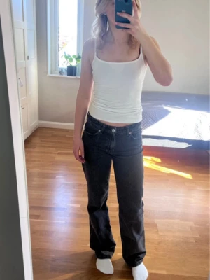 Svarta raka jeans - Säljer ett par svart/grå jeans med rak passform och normalhög midja. Jeansen har klassisk femficksdesign och stängs med knapp och dragkedja. Perfekta till en enkel topp eller hoodie för en avslappnad look.
