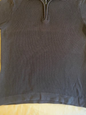 Mörkblå stickad tröja med halvzip - Mörkblå stickad tröja med halv dragkedja och krage. Tröjan har en enkel, ribbstickad struktur och raka ärmar. Perfekt för lager på lager och en clean look. Materialet känns mjukt och bekvämt.