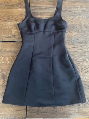 Svart kort klänning - En stilren svart klänning med figurnära passform. Perfekt för dig som gillar minimalistisk design och vill ha något enkelt men elegant.