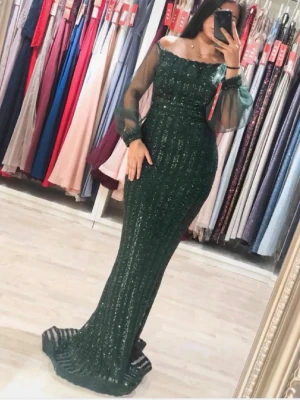 Mörkgrön glittrig långklänning aftonklänning strl S - Säljer en elegant mörkgrön långklänning med glittriga detaljer och transparenta långärmar. Klänningen har en figurnära passform och offshoulder-design som ger en lyxig känsla. Perfekt för dig som vill sticka ut på bal eller fest.