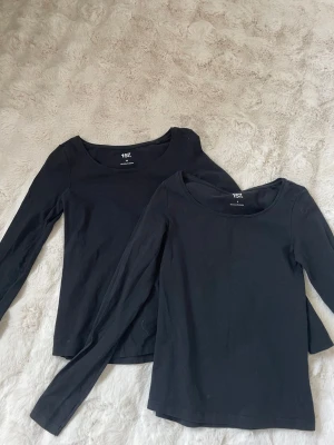 Svarta långärmade toppar 157 - Två svarta långärmade toppar från 157 med rund halsringning. Tillverkade i mjuk bomull, perfekta att styla med jeans eller kjol. Enkel och stilren design som passar till många olika looks. Den ena är S och den andra XS