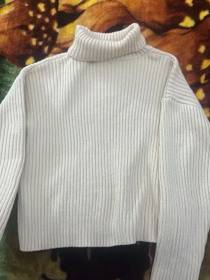 Beige ribbstickad polotröja - Säljer en beige ribbstickad med lång ärm och hög krage. Tröjan har en rak passform och är gjord i ett mjukt, stretchigt material som känns skönt mot huden. Perfekt för lager-på-lager och enkel att matcha med jeans eller kjol.