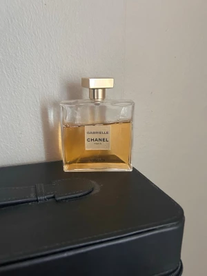 Chanel Gabrielle Essence parfym 100ml - Chanel Gabrielle Essence är en lyxig parfym i en elegant, fyrkantig glasflaska med guldig vätska och stilren etikett. Flaskan har en exklusiv, guldig kork och klassisk design som utstrålar tidlös elegans.