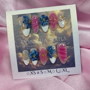 Petals (S);Medium Almond - Unika press-on naglar i en medium lång mandelform. Setet har en mix av rosa och nude bas med vita tippar, dekorerade med 3D-blommor i blått och guldiga detaljer. Några naglar har vita 3D-nailart för extra effekt. Perfekt för dig som vill sticka ut.Tack för inspo 💕 För att jag ska veta vad som kan passa: vilken längd och storlek vill du ha? XS–XL ✨
