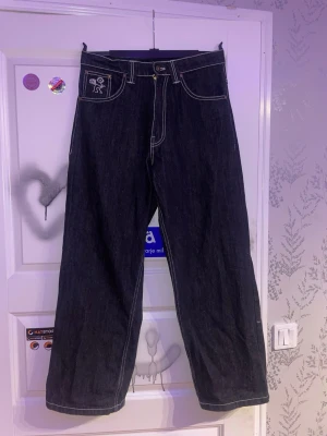 Svarta baggy jeans från bsat - Säljer ett par svarta baggy jeansjeans från bsat med kontrastsömmar och broderad logga på fickan fram. Jeansen har hög midja, raka ben och stora bakfickor. Perfekta för en avslappnad och trendig stil. Säljer då dom är för små för mig. Finns slitningar längst ner på bena se bild 3