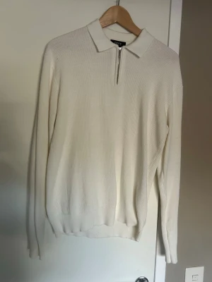 Vit stickad tröja med dragkedja - Snygg vit stickad tröja med krage och halv dragkedja framtill. Tröjan har lång ärm och ribbade muddar vid ärmslut och nederkant. Perfekt för en stilren och clean look.