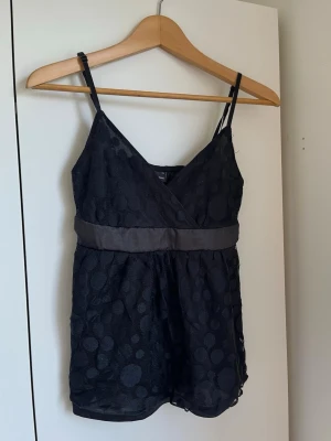 SPETSLINNE - Snygg svart topp från Gina Tricot med tunna axelband och v-ringnign. Toppen har ett brett satinband under bysten och ett prickigt spetslager. Perfekt att styla med jeans eller kjol för fest eller middag! Har använts ett antal gånger och något sliten i sömmarna. 