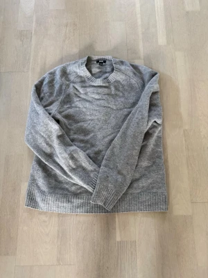 Grå cashmere-tröja från Uniqlo - Mjuk och stilren grå stickad tröja från Uniqlo i 100% cashmere. Tröjan har rund halsringning, långa ärmar och ribbstickade muddar vid ärmslut och nederkant. Perfekt för lager-på-lager och enkel att matcha med olika outfits. SITTER SOM EN S JAG ÄR 176 cm och 69kg förkort på mig! 