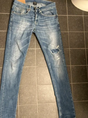 Ljusblå slitna slim jeans herr - Säljer ett par ljusblå slim jeans med slitningar och hål på ena benet. Jeansen har klassisk femficksdesign, dragkedjegylf och är i stretchigt denimtyg. Perfekta för en avslappnad streetstil.