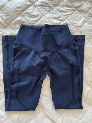Mörkblå tights från ICIW - Snygga mörkblå seamless tights från ICANIWILL med hög midja och scrunch-detalj bak. Tightsen har diskreta svarta ränder längs benen. Färgen ser lite mer lila ut i verkligheten, knappt använda