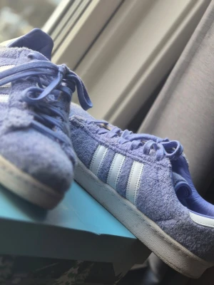 Lila Adidas Campus 80s x South Park - Unika och ovanliga lila Adidas Campus 80s x South Park Towelie sneakers med mjuk handduks liknande ovandel med de klassiska vita ränder på sidorna. Skorna har matchande lila skosnören med cigarette liknande design på varje ände. Perfekt för dig som vill sticka ut med en färggladl stil eller för dig som samlar på ovanliga eller speciella skor.